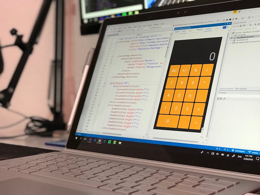 A close-up view of a laptop computer placed on a desk, displaying a code editor with HTML and CSS code on the left side of the screen and a large digital calculator interface with orange buttons on th